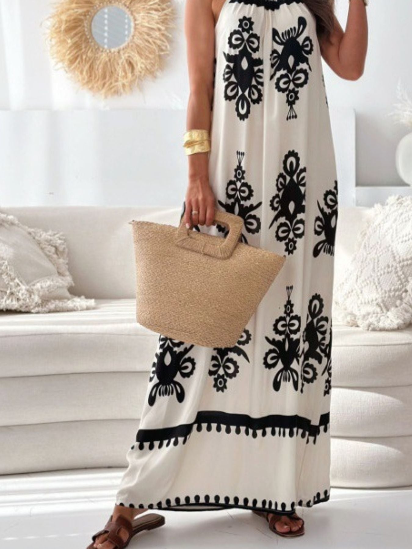 Woman wearing a white dress with black patterns, holding a beige bag in a living room.