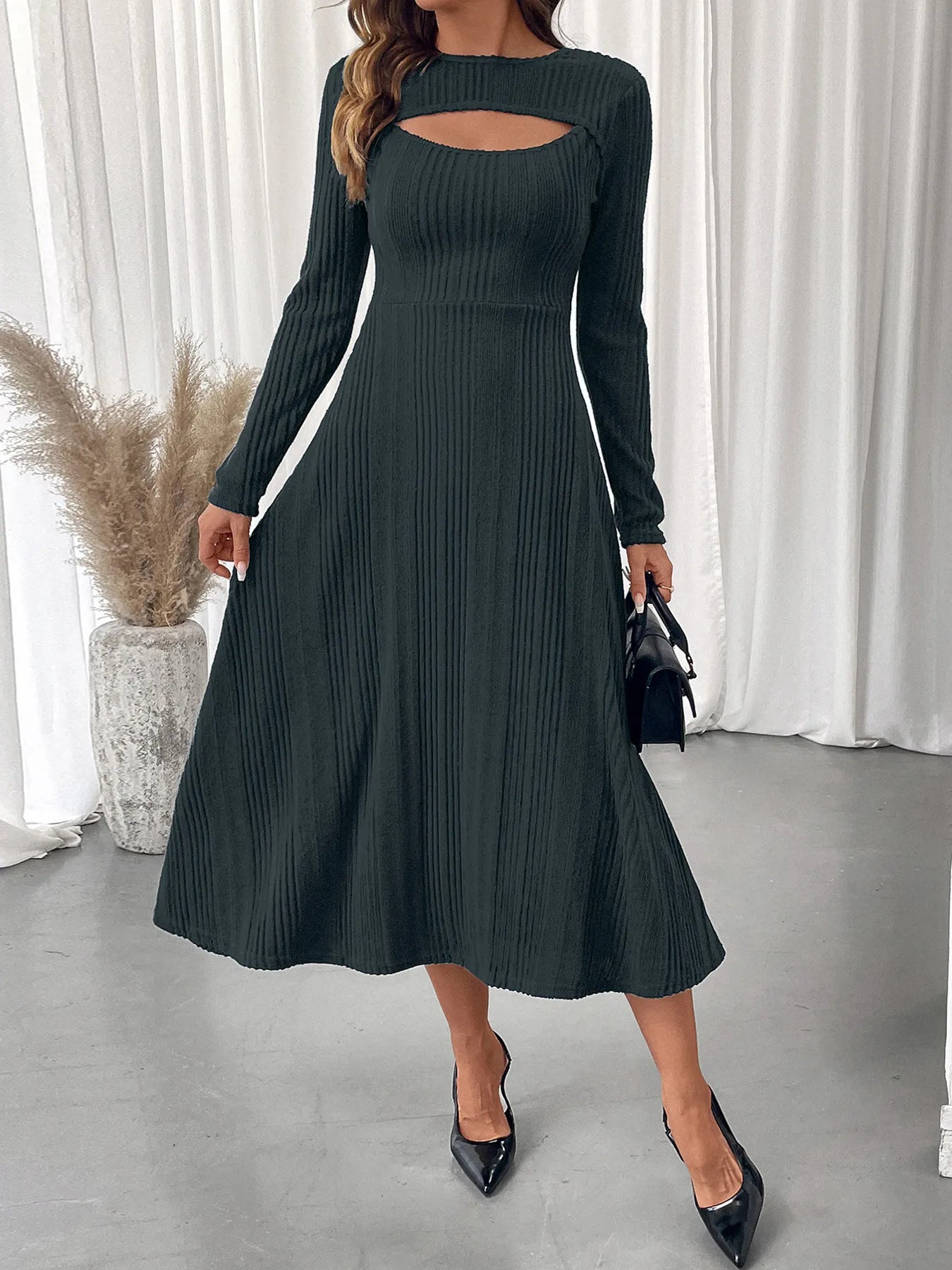 Woman wearing a green ribbed dress with cut-out design in a minimalistic setting.
