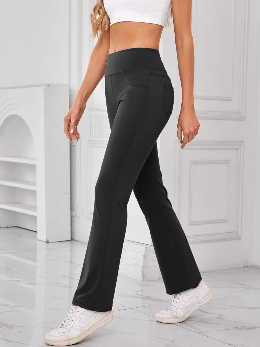 Person wearing black flared pants and white sneakers in a minimalistic setting