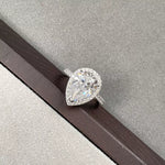 Pear-shaped diamond ring on a wooden surface with a gray background