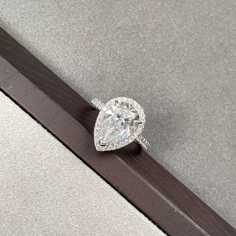 Pear-shaped diamond ring on a wooden surface with a gray background