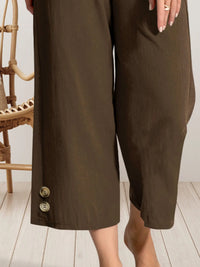 Brown pants with buttons worn by a person on a light wooden floor.