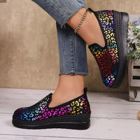 Multicolored leopard print shoes worn with blue jeans on a wooden floor.