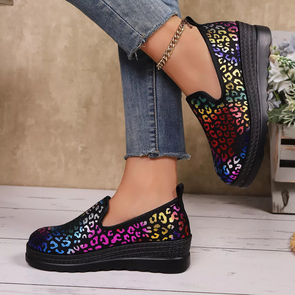Multicolored leopard print shoes worn with blue jeans on a wooden floor.