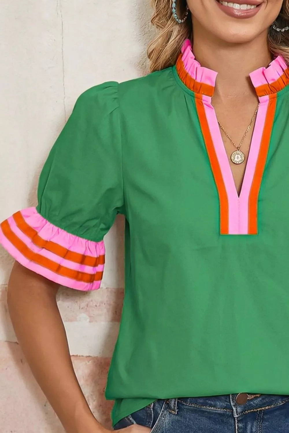 Green blouse with colorful trim worn by a person, against a neutral background
