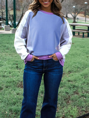 Person wearing a two-tone sweatshirt with purple sleeves and white body, standing in a park.