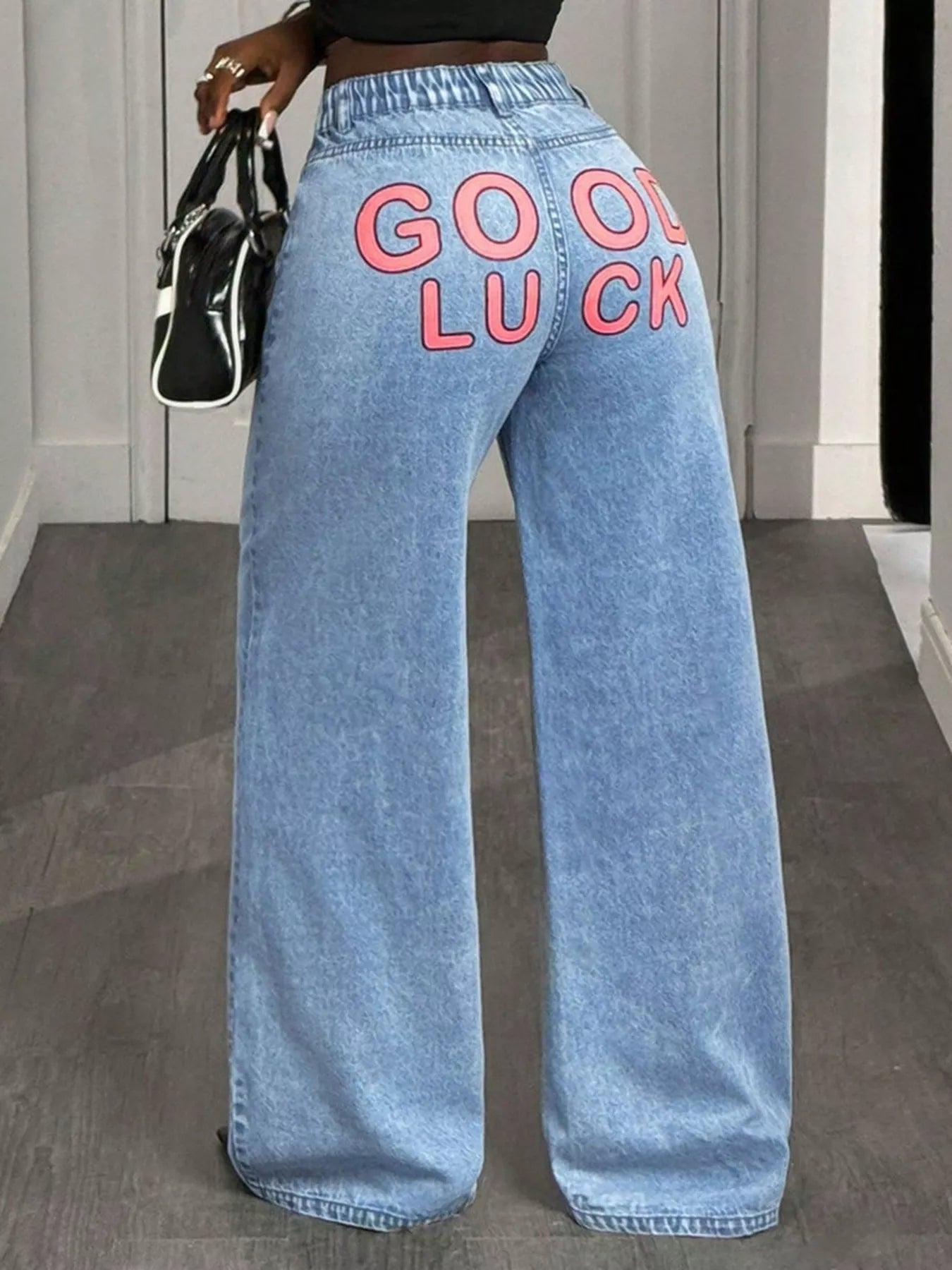 Person wearing light blue jeans with 'GOOD LUCK' text, standing indoors.
