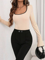Woman wearing a beige long-sleeve top and black pants against a white background