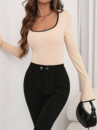 Woman wearing a beige long-sleeve top and black pants against a white background