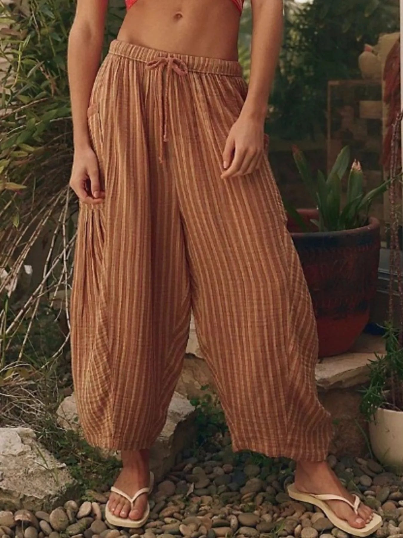 Person wearing brown striped pants standing outdoors with plants in the background