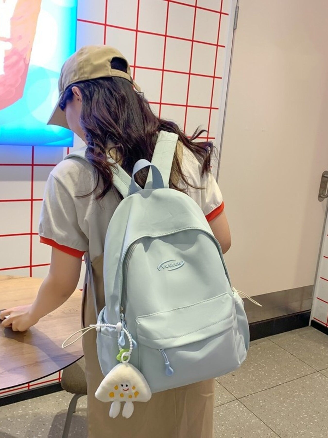 Person wearing a light blue backpack with a small plush toy, standing in a casual setting.