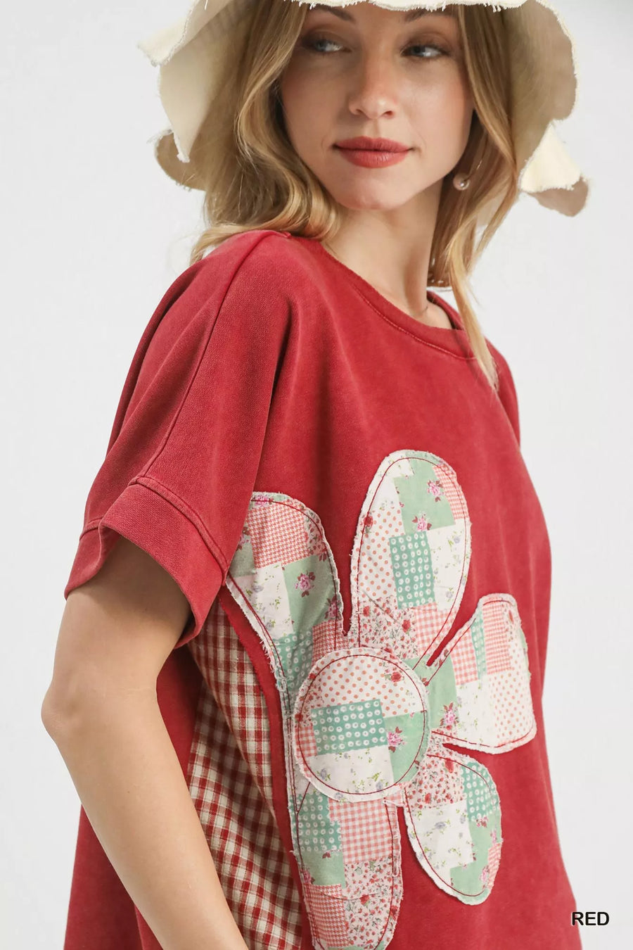 Woman wearing a red t-shirt with a floral patch design on a plain background