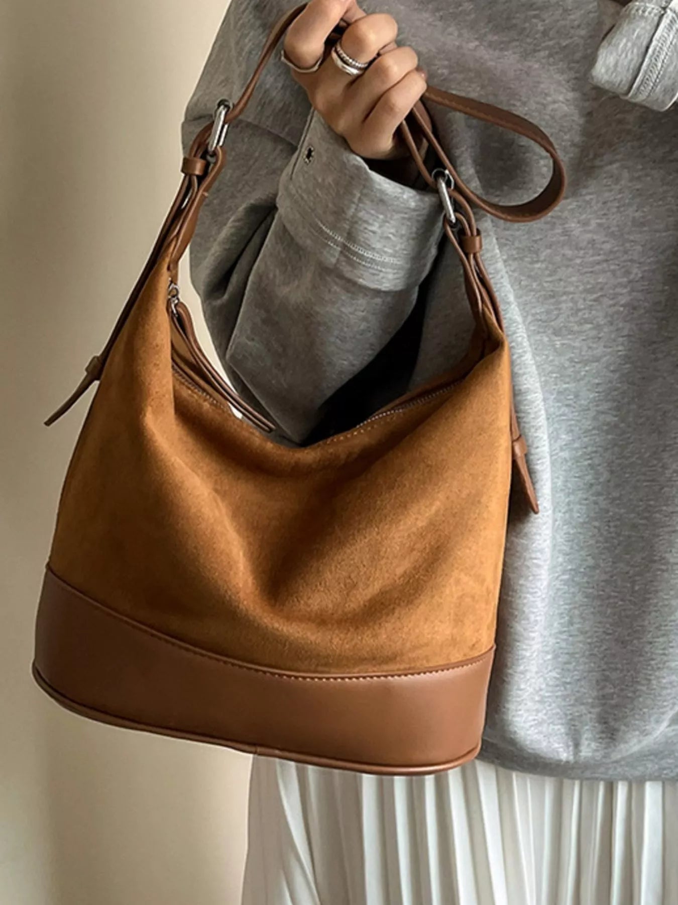 Brown handbag held by a person wearing a gray sweater.