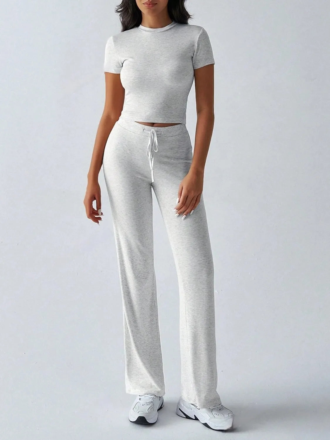 Person wearing a gray crop top and pants set on a white background