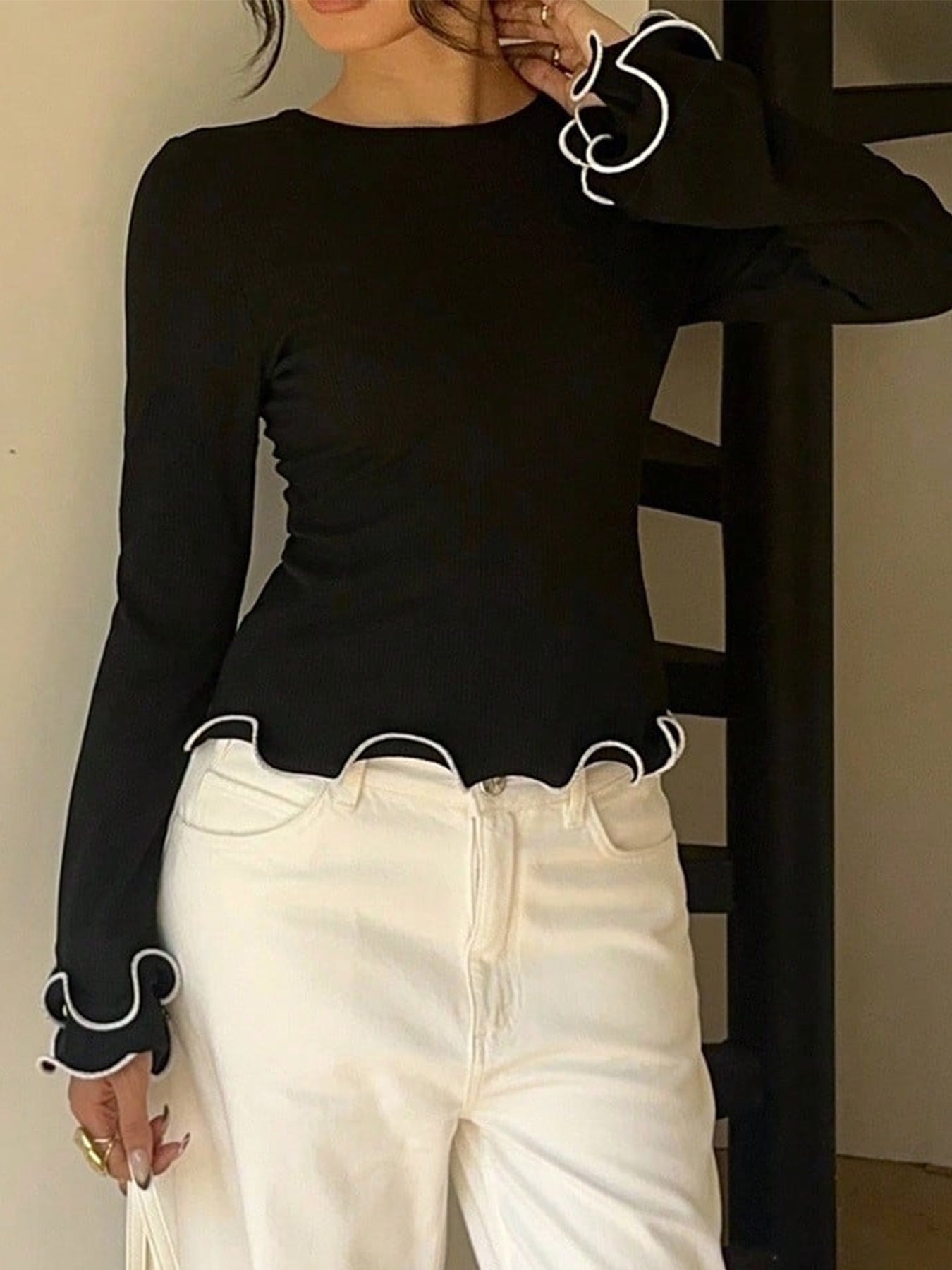 Person wearing a black long-sleeve top with white trim and white pants, standing against a neutral background.