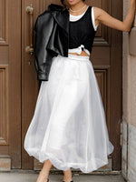 Person wearing a black leather jacket, black top, and white skirt standing in front of a wooden door.