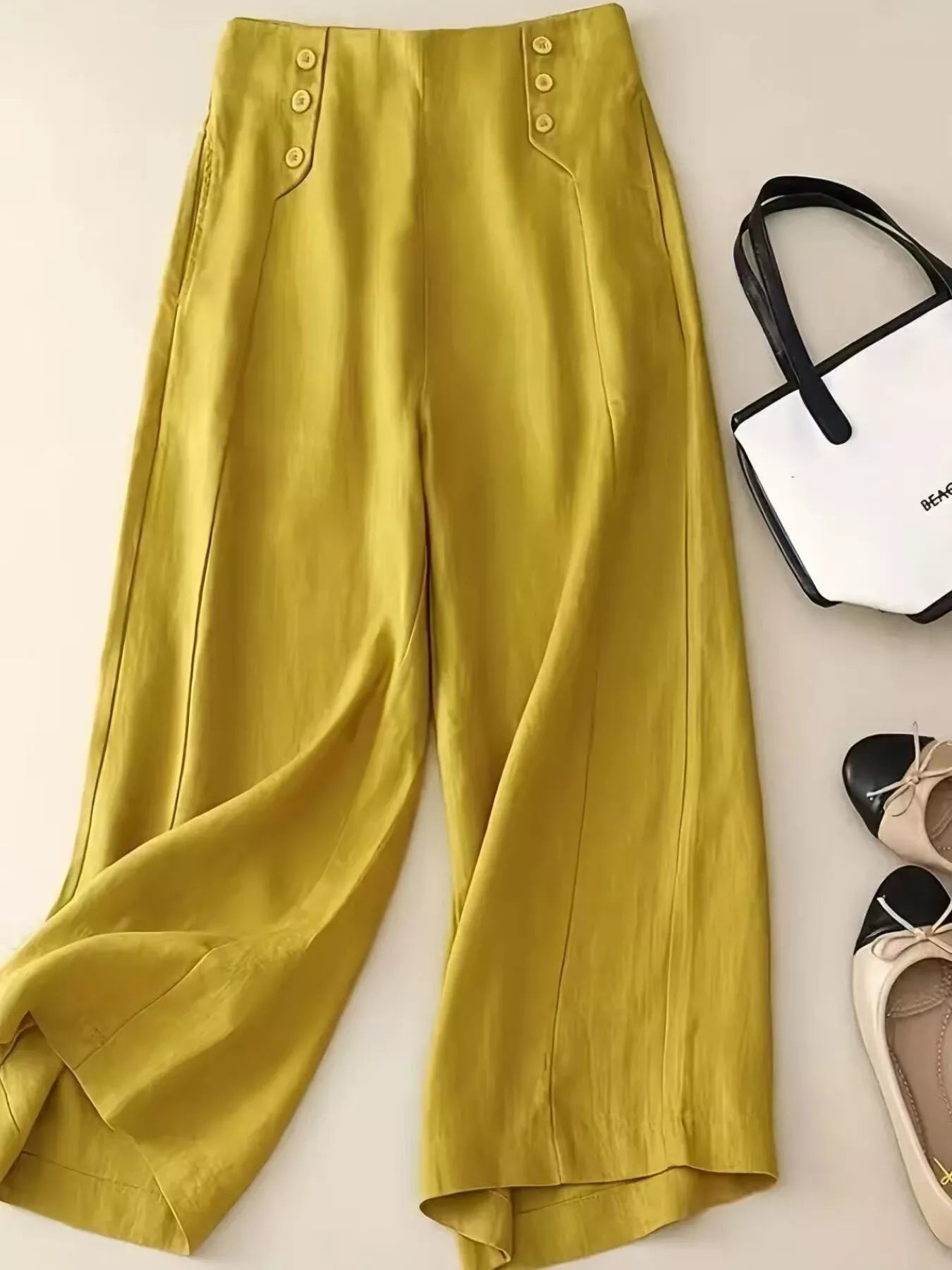 Yellow pants displayed on a white surface with a handbag and shoes.