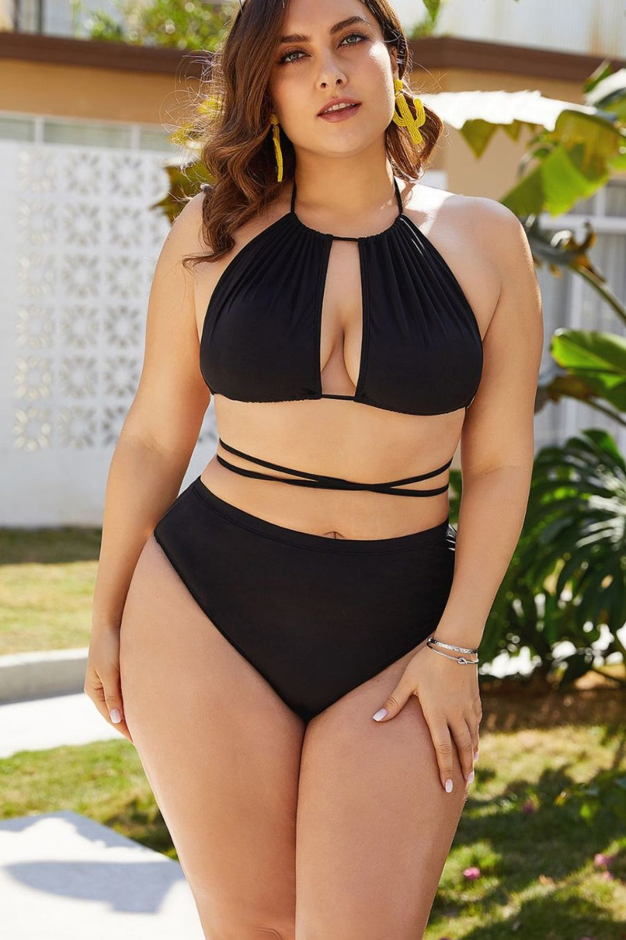 Woman wearing a black bikini set outdoors with greenery in the background