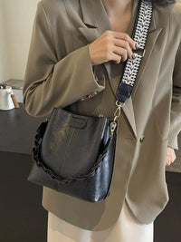 Person holding a black handbag with a chain detail, wearing a beige suit.