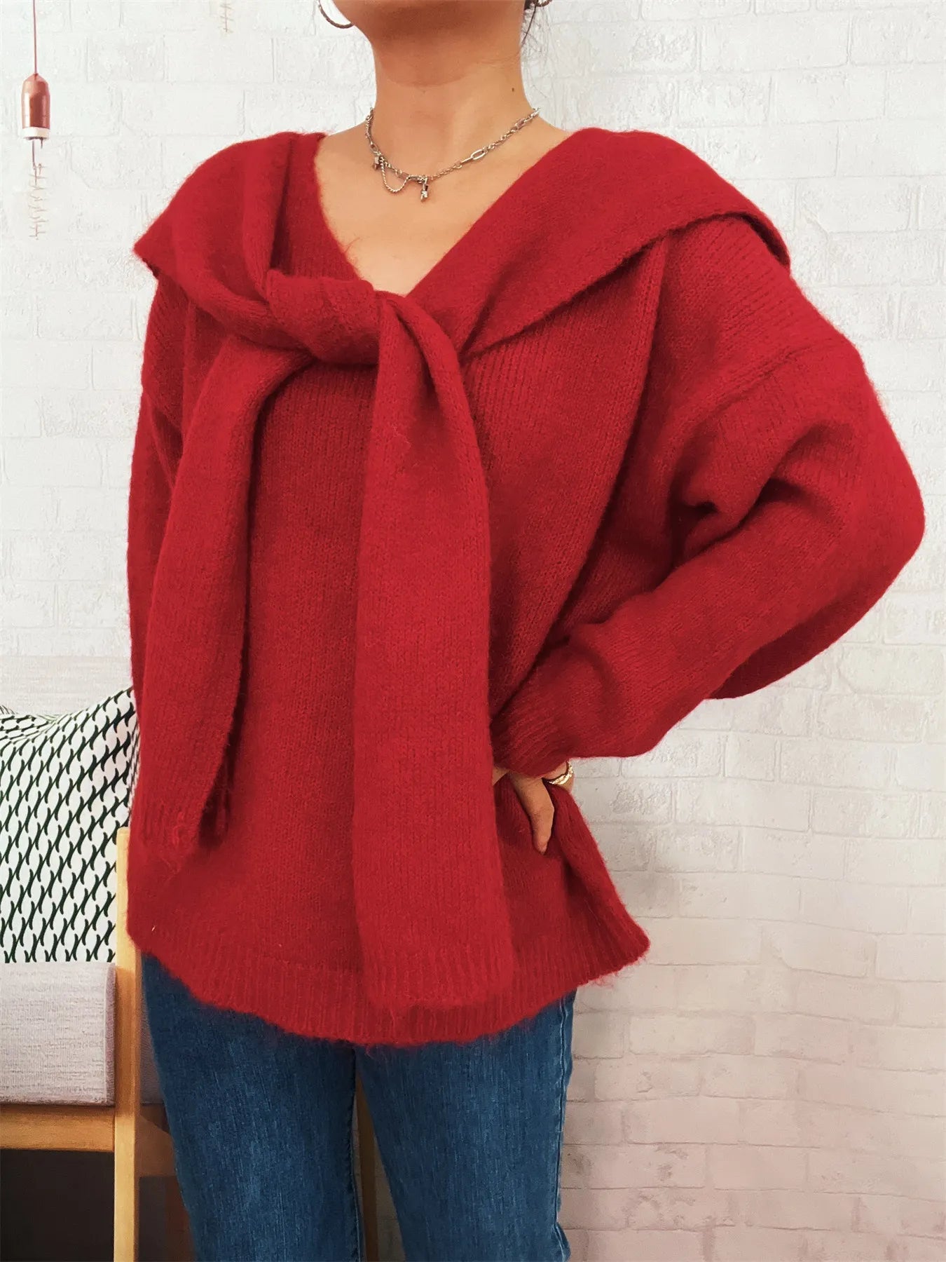Person wearing a red sweater with a hood against a white brick wall.