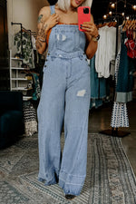 Person wearing a denim jumpsuit taking a mirror selfie in a clothing store.