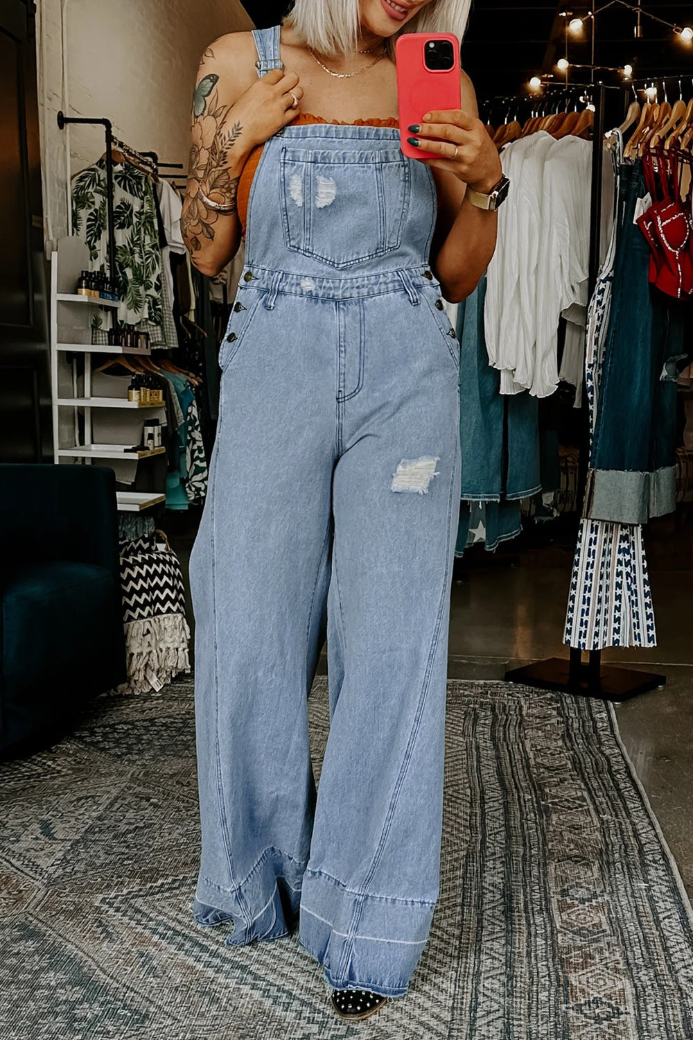 Person wearing a denim jumpsuit taking a mirror selfie in a clothing store.