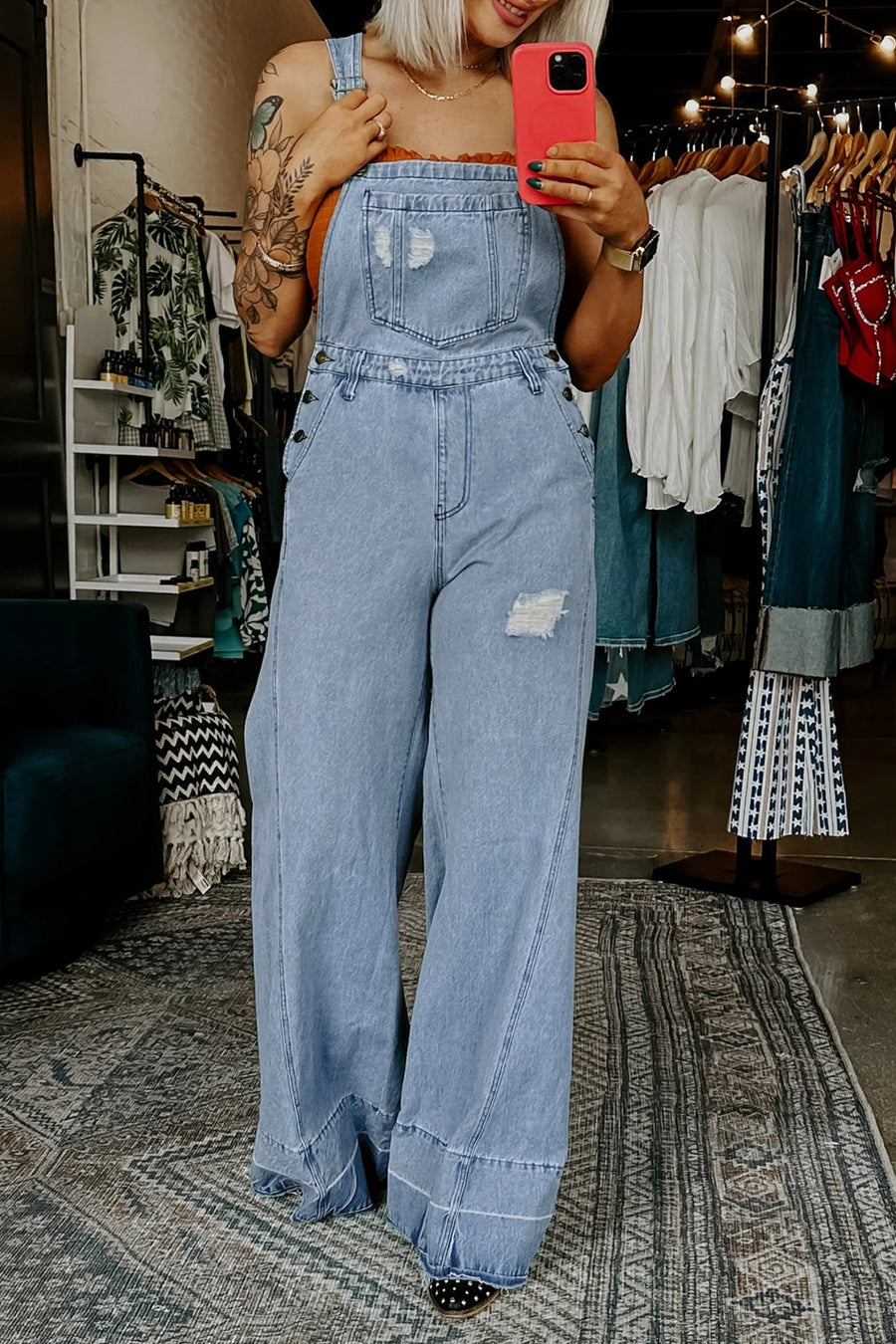 Person wearing a denim jumpsuit taking a mirror selfie in a clothing store.