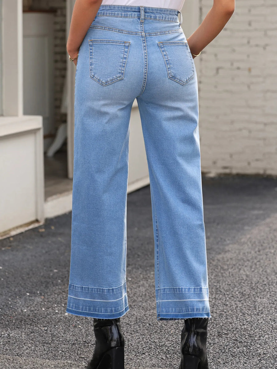 Person wearing light blue jeans standing on a street with a white building in the background