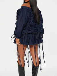 Navy off-shoulder dress with ruched details and long boots on a white background