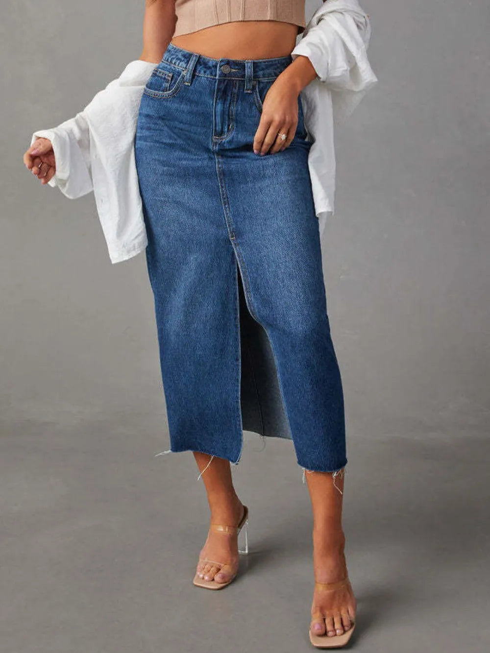Person wearing a long blue denim skirt with a plain background