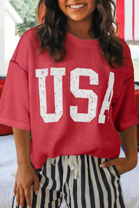 Person wearing a red 'USA' shirt with striped pants indoors.