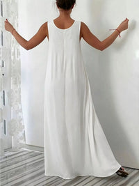 Woman wearing a long white dress with arms outstretched in a minimalistic setting.