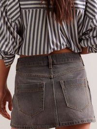 Person wearing a striped shirt and denim skirt on a plain background