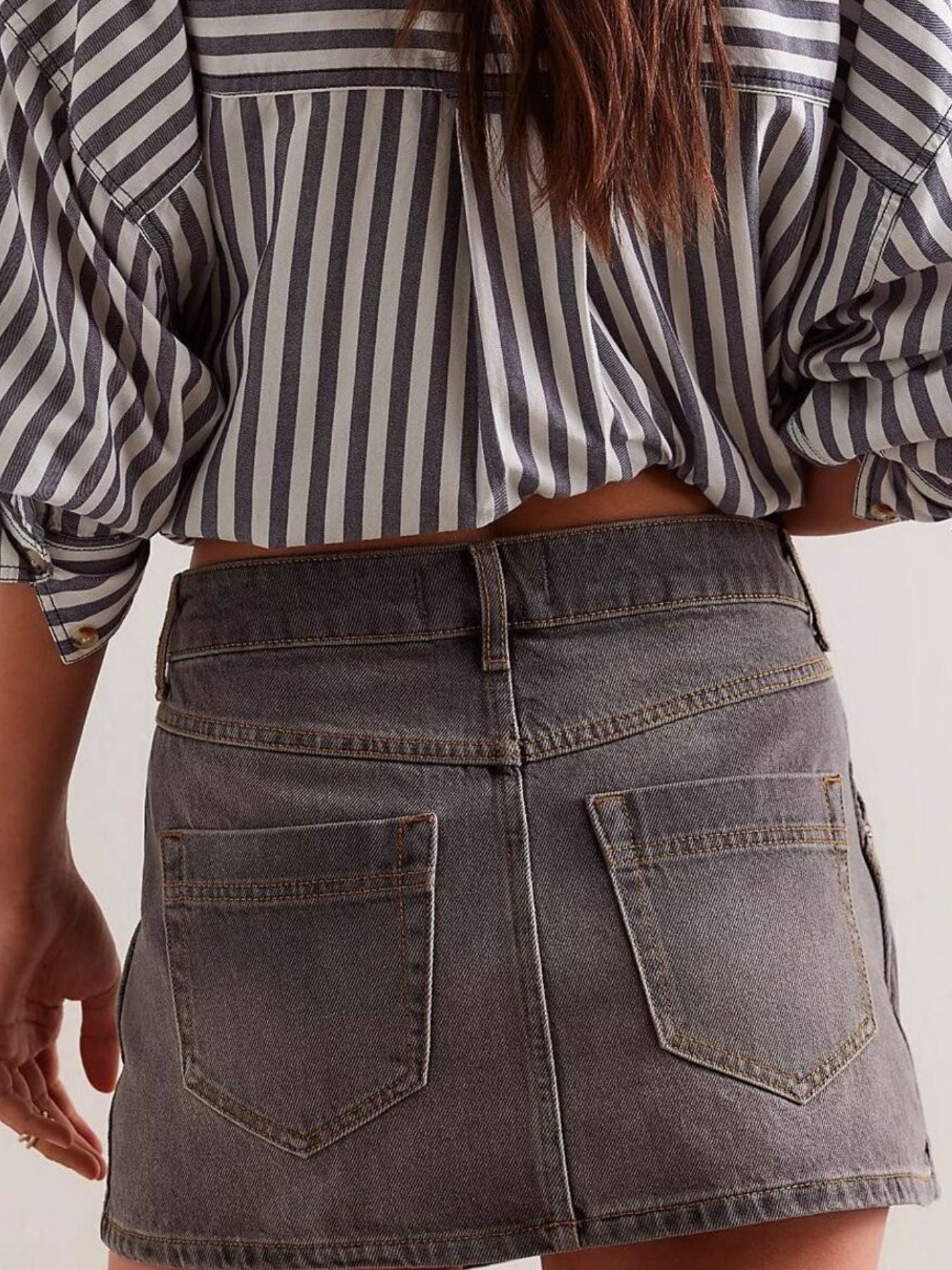 Person wearing a striped shirt and denim skirt on a plain background