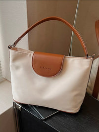 Beige handbag with brown leather patch on a dark surface