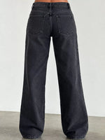 Back view of a person wearing dark charcoal wide-leg jeans with a straight-to-relaxed leg and back pocket design, standing against a plain light gray wall.