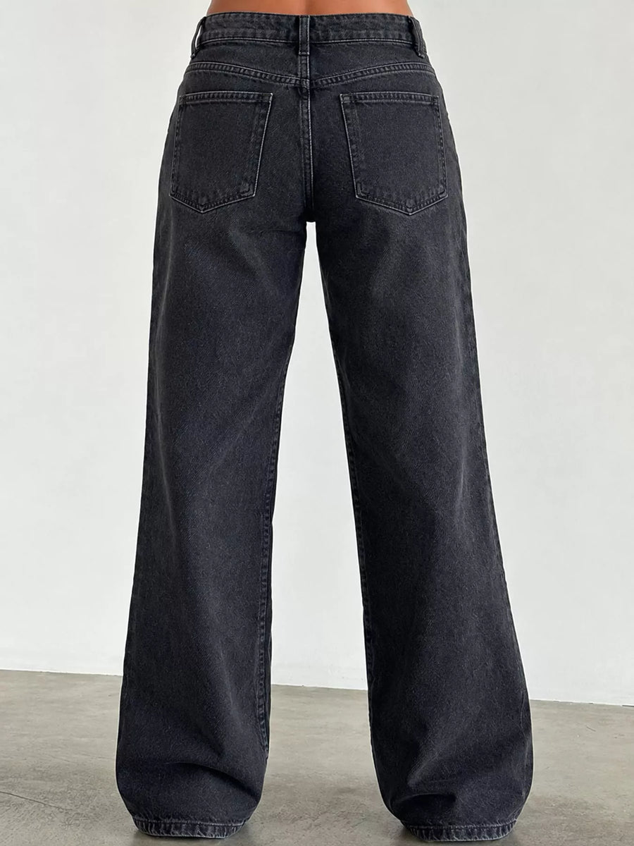 Back view of a person wearing dark charcoal wide-leg jeans with a straight-to-relaxed leg and back pocket design, standing against a plain light gray wall.