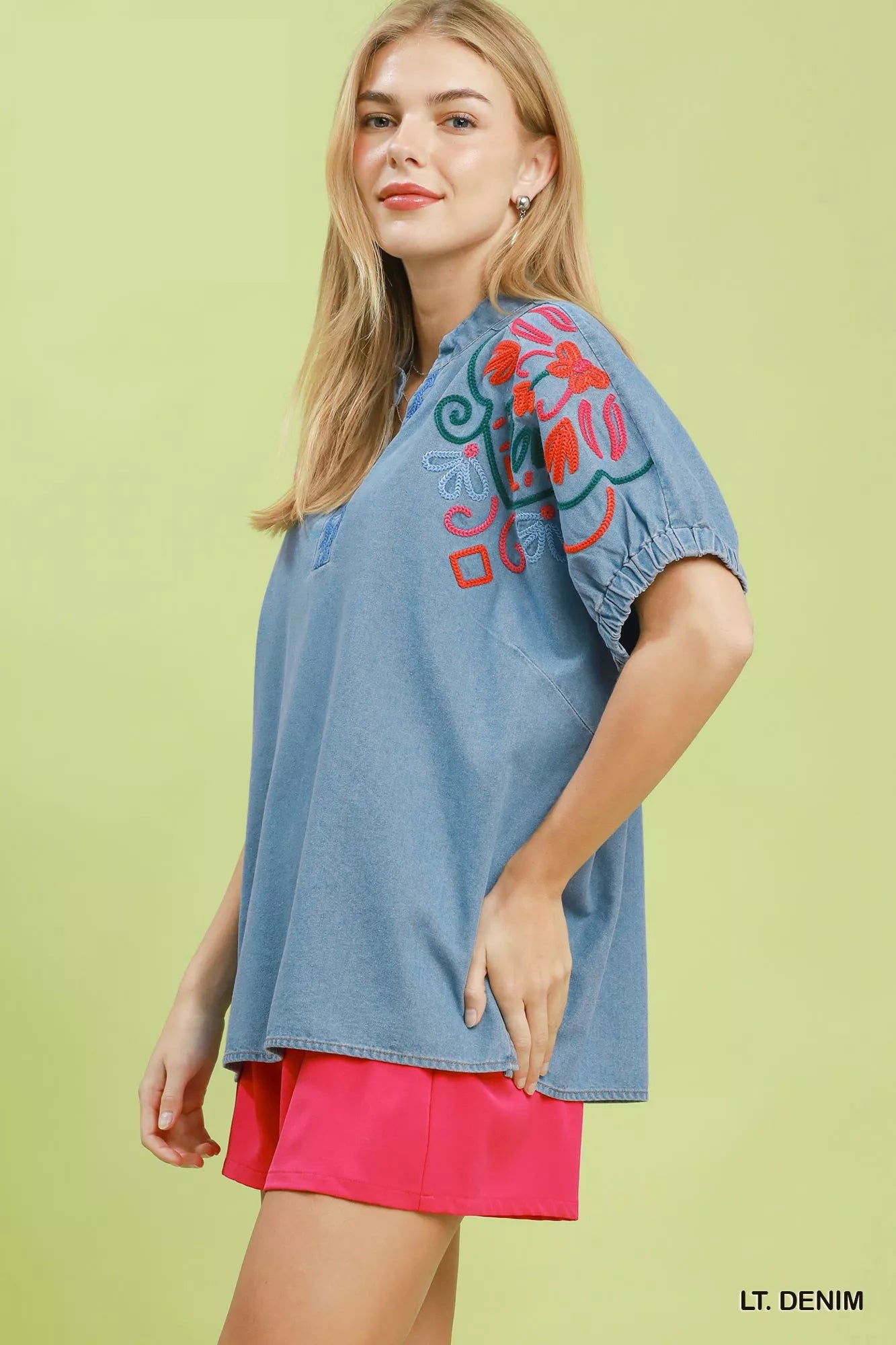 Woman wearing a light denim top with red embroidery on a light green background