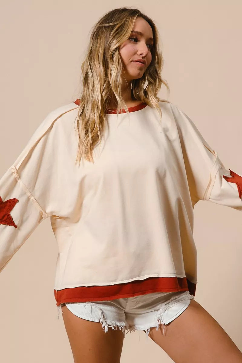 Woman wearing a white oversized sweater with red accents and denim shorts on a beige background