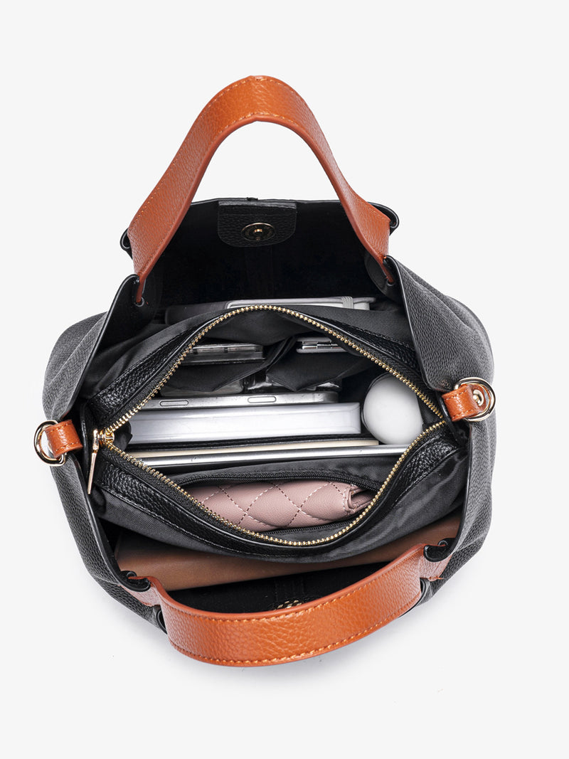 Black handbag with brown leather accents open to reveal its contents on a white background