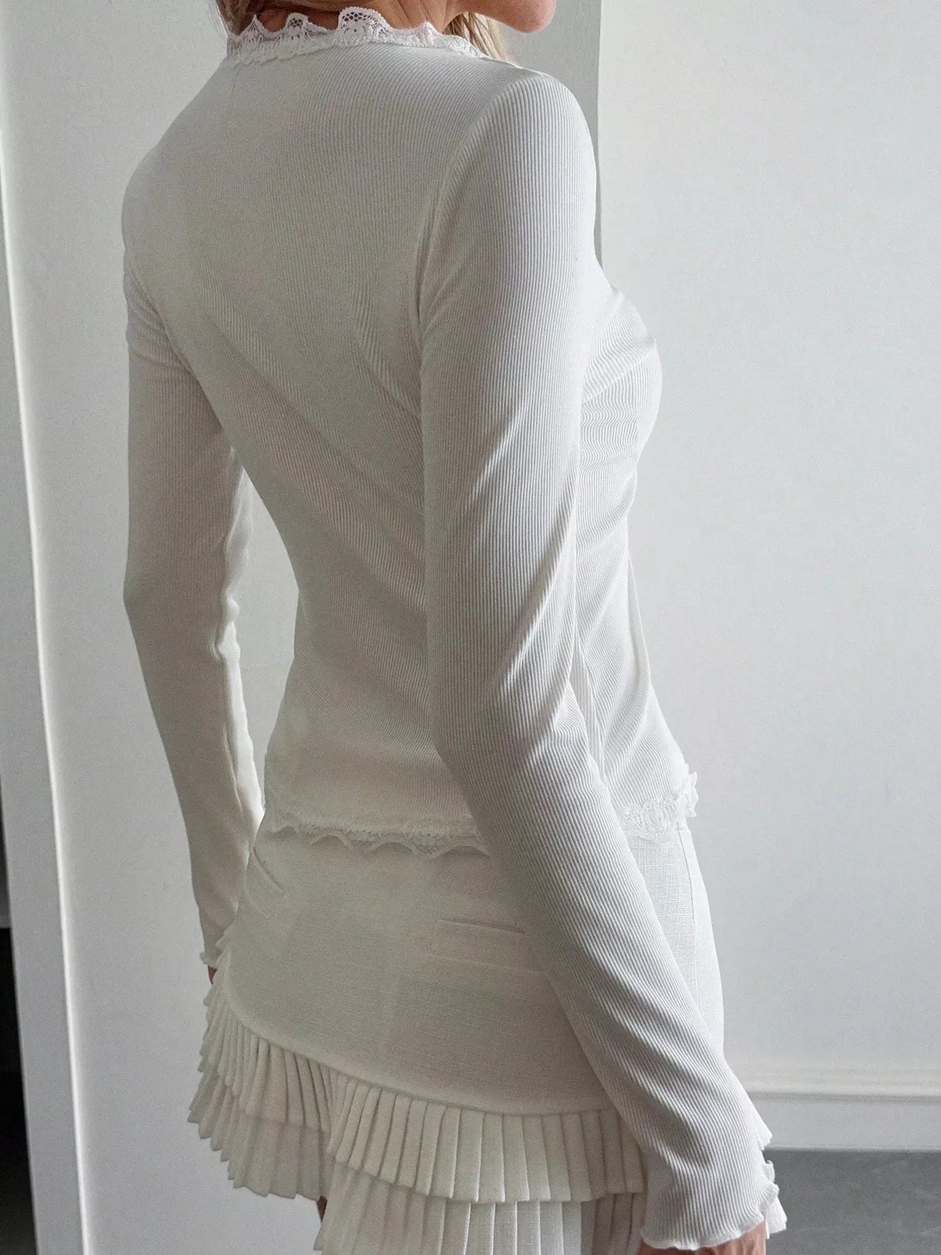 White long-sleeve top with lace neckline and pleated skirt against a white background