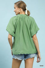 Woman wearing a green blouse and denim shorts against a light blue background