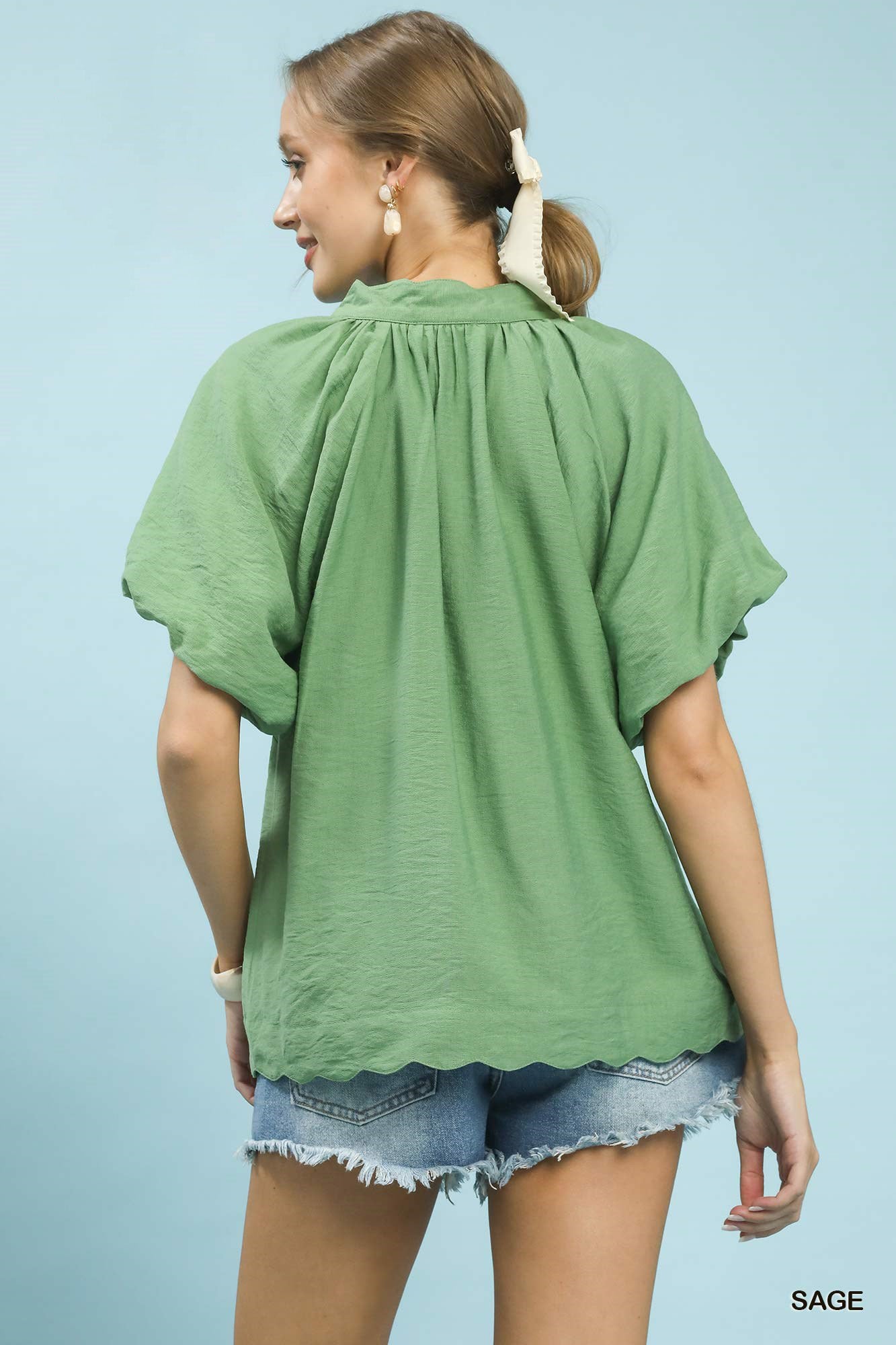Woman wearing a green blouse and denim shorts against a light blue background