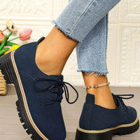 Navy blue shoes with black laces worn with light blue jeans against a textured wall.