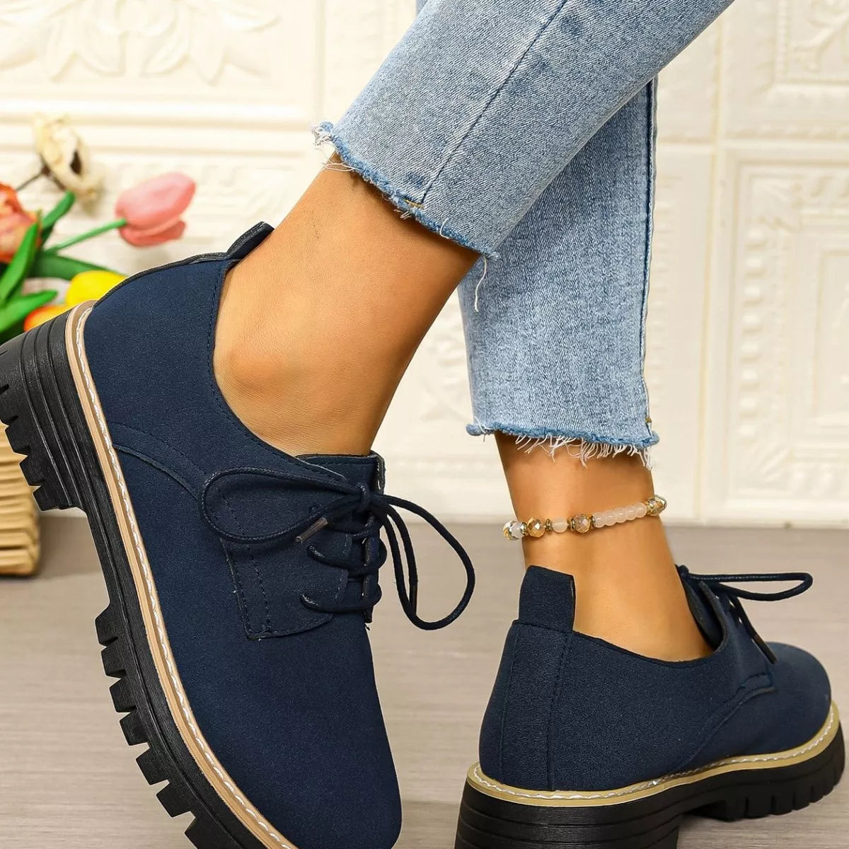 Navy blue shoes with black laces worn with light blue jeans against a textured wall.