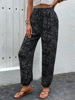 Person wearing black patterned pants against a light gray wall.