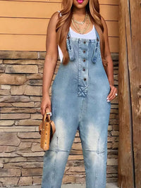 Woman wearing a denim jumpsuit standing against a stone wall.