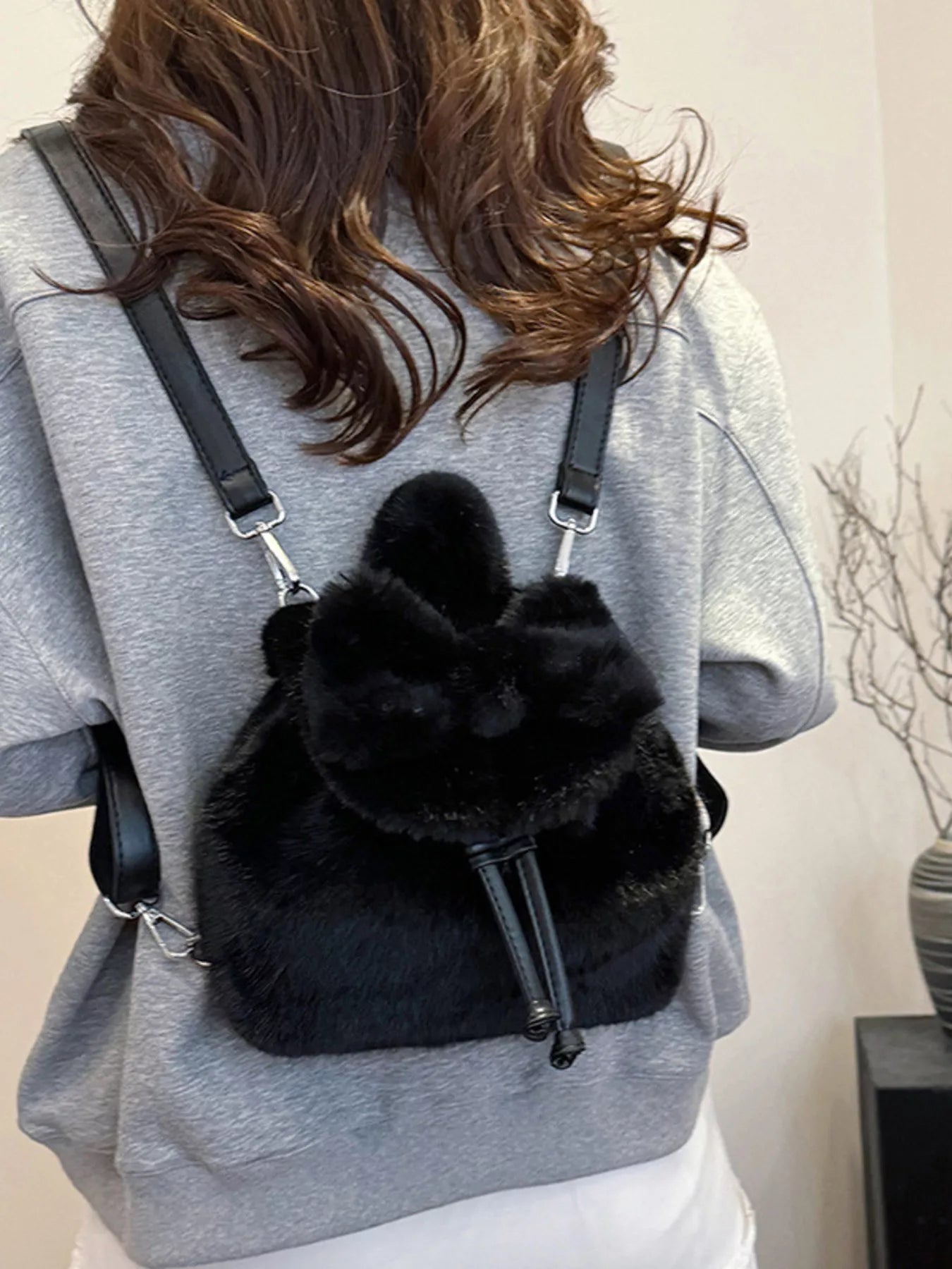 Person wearing a black fluffy backpack with a plain background