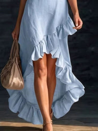 Woman wearing a light blue ruffled dress holding a beige handbag on a dark background