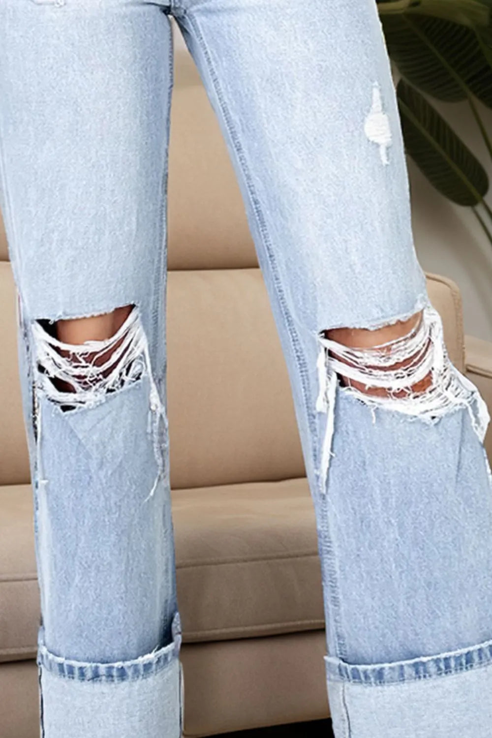 Light blue ripped jeans with lace inserts worn by a person, sitting on a beige couch.